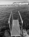 Black and white image of motorboats in the ocean harbour with metal stairs and handrails