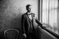 Black and white photo with noise. brooding groom standing near the window.