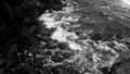 Black and white photo of ocean waves rolling and breaking on sharp cliffs and rocks on the beach