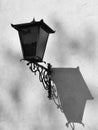 Black and white photo of old fashion vintage orange streetlight with cast iron frame on the white wall of the house.
