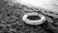 Black and white image of plastic life saving ring lying on the sea beach. Concept of safety during summer holiday Royalty Free Stock Photo