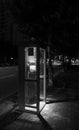 Black and white photo of the public telephone booth lighting up the dark night road alone. Royalty Free Stock Photo