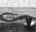 Black and white photo of a silver espresso cup and coffee beans on wooden table. Royalty Free Stock Photo
