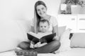 Black and white photo of smiling young mother with baby boy reading big old book Royalty Free Stock Photo