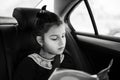 Black and white photo of teenage girl reading a book inside car.