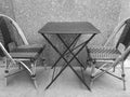Black and white photo of two cafe chairs and table outdoors