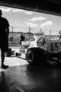 Black and White Photo of a Vintage Race Car In a Pitstop Garage.