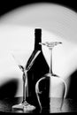 Black and white photo of a wine bottle and two glasses against the light spot on the black wall Royalty Free Stock Photo