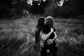 Black and white photo of woman with son in her arms on dry grass field and forest background. Happy mom with long dark Royalty Free Stock Photo