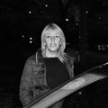 black and white photo of woman waiting behind a car.
