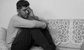 Depressed young man sitting on sofa at home in black and white