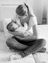 Black and white photo of young owman sitting on bed and holding her sleeping baby Royalty Free Stock Photo