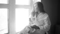 Black and white photo of young woman in bathrobe drinking coffee at big window Royalty Free Stock Photo