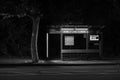 Black and white picture of the bus stop at a late hour.