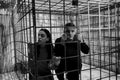 Black and white picture of couple afraid Halloween victims imprisoned in a metal cage looking out through the bars