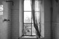 Black and white picture of a depressive dirty bathroom in an abandoned house of Chernobyl. Broken window with old curtain.