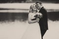 A black and white picture of a happy wedding couple standing behind a lake