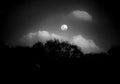 A black and white picture of moon in between the clouds