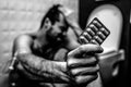 Black and white picture of young man sit on floor in rest room and hold plate of pills. Hand is wrapped with plait for Royalty Free Stock Photo