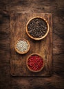 Black, white and pink rose peppers in bowls, assorted spices and spicy herbs on wooden rustic kitchen table, copy space, top view Royalty Free Stock Photo