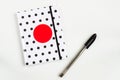 Black and white polka dot note book with red circle  on the cover and black pen on white table. top view, minimal flat lay Royalty Free Stock Photo