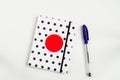 Black and white polka dot note book with red circle  on the cover and blue pen on white table. top view, minimal flat lay Royalty Free Stock Photo