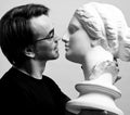 Black and white portrait of adult man in black t-shirt holding in hands antique sculpture woman head, going to kiss it