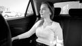 Black and white portrait of beautiful elegant smiling woman sitting on car back seat and looking out of the open window Royalty Free Stock Photo