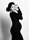 Black and white portrait of beautiful pregnant woman posing side to us in tight dress holding hands at head, looking at camera Royalty Free Stock Photo