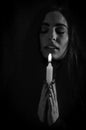 Black and white portrait of a beautiful young woman with long hair holding a lit candle in her hand and praying with closed eyes Royalty Free Stock Photo