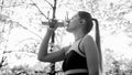 Black and white portrait of beautiful young woman in sports outfit drinking water from bottle after exercising in park Royalty Free Stock Photo