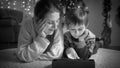 Black and white portrait of boy with mom lying on floor and using tablet computer next to Christmas tree at living room. Royalty Free Stock Photo