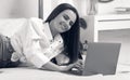 Black and white portrait of casual girl smiling and using laptop while laying in bed Royalty Free Stock Photo