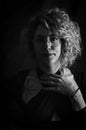 Black and white portrait of a curly blonde woman with eyeglasses who looks confused with her hand on her chest Royalty Free Stock Photo