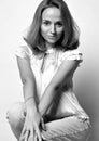 Black and white portrait of flirty smiling young sexy woman with long blonde hair in blouse and jeans sitting squatted Royalty Free Stock Photo