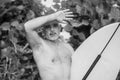 Black and white portrait of handsome shirtless man surfer, holding white surf board and cactus on background