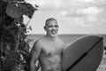 Black and white portrait of handsome shirtless man surfer, holding white surf board and cactus on background