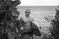 Black and white portrait of handsome shirtless man surfer, holding white surf board and cactus on background