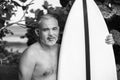 Black and white portrait of handsome shirtless man surfer, holding white surf board and cactus on background