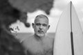 Black and white portrait of handsome shirtless man surfer, holding white surf board and cactus on background