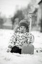 Black and white portrait of little boy in winter clothes sitting in snow with shovel in hand. Thoughtful, pensive look Royalty Free Stock Photo