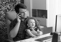 Black and white portrait of young man working in office talking by phone and holding his baby son Royalty Free Stock Photo