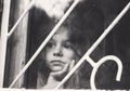 Black and white portrait of Sad little girl looks through window