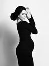 Black and white portrait of young noble pregnant woman standing side to us in black elegant dress holding hands at head Royalty Free Stock Photo