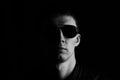 Black and white portrait of serious young man in a black leather jacket and sunglasses isolated on black background Royalty Free Stock Photo