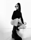 Black and white portrait of sexy brunette woman in black string bodysuit, brutal shoes and sunglasses sitting squatted