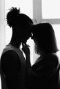 Black and white portrait, silhouette of a multiracial couple, boyfriend and girlfriend face to face, stand at the window