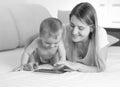 Black and white portrait of smiling mother and baby using digital tablet on bed Royalty Free Stock Photo