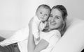 Black and white portrait of smiling young woman lying on bed and holding her 3 months old baby boy Royalty Free Stock Photo