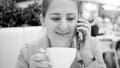 Black and white portrait of smilng young woman drinking coffee and talking by phone